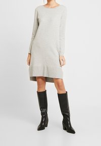 Abito a maniche lunghe grigio in maglia con scollatura rotonda e orlo a coste, abbinato a stivali neri al ginocchio con tacco a blocco.