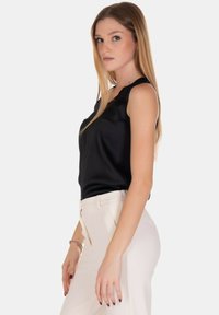 Top in satin nero con aperture sulle spalle, abbinato a pantaloni a vita alta color crema con zip laterale e fit slim.