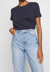 Navy blue cotton t-shirt with a crew neckline and short sleeves, paired with high-waisted light blue denim jeans with a relaxed fit.