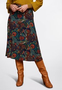 Jupe à motifs floraux en bleu foncé et vert, avec des accents rouges et canards. Associée à des bottes marron jusqu'aux genoux. Coupe lisse de longueur intermédiaire.