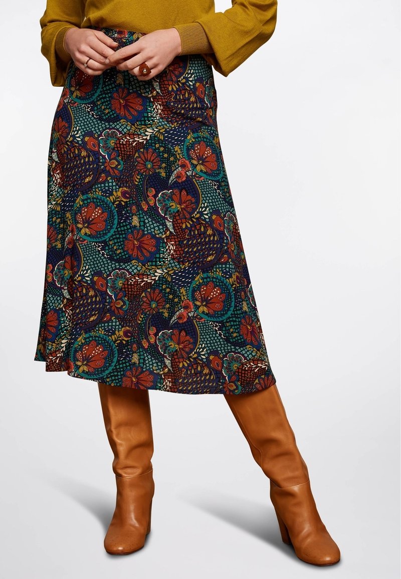Jupe à motifs floraux en bleu foncé et vert, avec des accents rouges et canards. Associée à des bottes marron jusqu'aux genoux. Coupe lisse de longueur intermédiaire.
