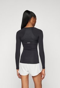 Haut de sport noir à manches longues avec une coupe ajustée, des panneaux texturés et des finitions à coutures planes, arborant un logo "TECHFIT" blanc au dos.