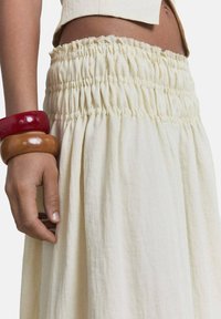 Falda color crema con detalle de cintura fruncida. Presenta una tela suave y fluida. Los accesorios incluyen tres pulseras gruesas en varios colores.