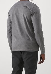 Graues Langarmshirt aus weichem Stoff, mit rundem Ausschnitt und kleinem schwarzen Logo auf dem oberen Rücken.