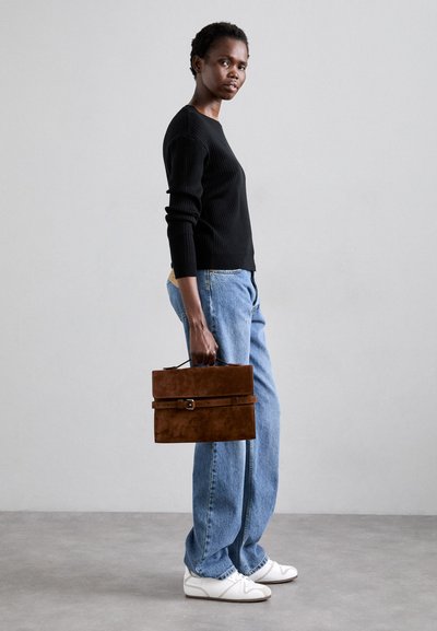 Geantă rectangulară din suede maro, cu mânere superioare și închidere tip curea, purtată împreună cu un pulover negru cu dungi și blugi ușor albaștri.