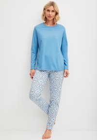 Lichtblauwe blouse met lange mouwen gecombineerd met aansluitende broeken met een ingewikkeld patroon in tinten blauw en wit. Zachte stof en een relaxte pasvorm.