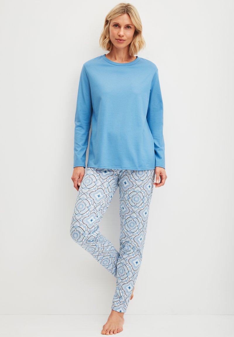 Lichtblauwe blouse met lange mouwen gecombineerd met aansluitende broeken met een ingewikkeld patroon in tinten blauw en wit. Zachte stof en een relaxte pasvorm.