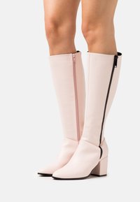 Knöchelhohe, blassrosafarbene Stiefel aus glattem Kunstleder mit einem seitlichen Reißverschluss und Blockabsatz, versehen mit einem schwarzen Reißverschlussakzent.