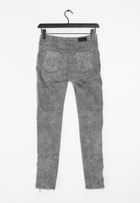 Jeans ajustados de tela gris con un estampado floral, que cuentan con una waistband de altura media, dos bolsillos traseros y cremalleras en el tobillo.