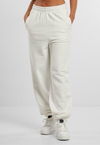 Hvide, bløde, højtaljede sweatpants med elastisk talje, sidelommer og tapered manchetter. Kombination med hvide sneakers.