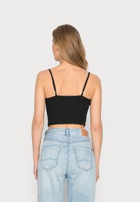 Top cropped preto com alças finas e hem médio recortado, combinado com jeans de cintura alta azul claro com um patch de couro e bolsos traseiros curvados.