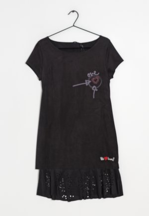 Czarna sukienka z krótkim rękawem, z motywem serca i strzały na piersi oraz wycinankami laserowymi na dolnym brzegu, zawieszona na czarnym wieszaku.