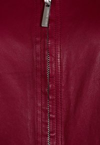 weinfarbene Lederjacke mit einem zentralen Reißverschluss und metallischem Zug, genähten Details entlang der Kanten und einer glatten Textur.