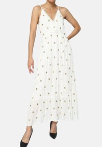 Robe maxi blanche avec broderie florale dorée. Dotée d'un décolleté en V, de bretelles ajustables et d'une jupe à volants. Tissu lisse avec un design léger.