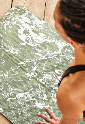 Green yoga mat featuring a textured surface with white marbled patterns and subtle ribbing, positioned on a wooden floor.