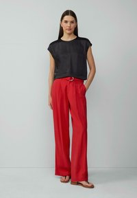 Haut noir à manches courtes avec une coupe décontractée, associé à un pantalon large taille haute rouge doté d'une boucle de ceinture circulaire en argent.