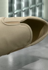 Μπεζ παντόφλα από ύφασμα με στρογγυλεμένη μύτη και ραμμένα άκρα, που διαθέτει άνοιγμα στην κορυφή για εύκολο σκύψιμο και βγάλσιμο.
