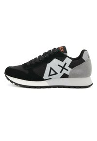 Zapatilla en negro y gris con materiales de ante y malla, que cuenta con una entresuela blanca, suela de goma y diseños de logotipos geométricos.