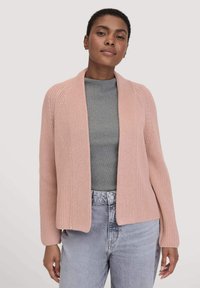 Großer Strickcardigan in sanftem Rosa, offenes Design mit geripptem Muster und langen Ärmeln, kombiniert mit einem grauen Hemd und hellgrauen Jeans.