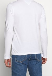 Weißes Langarmhemd mit weicher Textur und Rundhalsausschnitt, kombiniert mit blauen Jeans im klassischen Fünf-Taschen-Design.