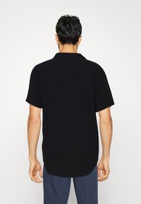 Chemise noire à manches courtes en tissu léger, présentant une coupe décontractée et un col classique, avec une texture lisse.