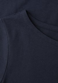 Gros plan sur un T-shirt en coton bleu marine montrant l'encolure ronde et les détails de couture de la couture d'épaule.