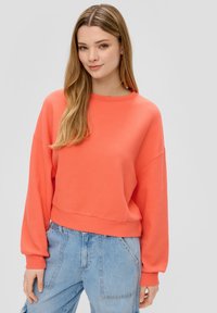 Sweatshirt surdimensionné en corail avec un tissu texturé, un col rond et des manches longues. Associé à un jean en denim taille haute de couleur bleu clair.