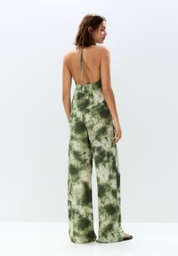 Grön tie-dye jumpsuit med en rygglös design, med vida byxor och en avslappnad passform. Tillverkad av lätt tyg med en mjuk textur.