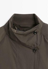 Braune Jacke mit hohem Kragen und doppelter Knopfverschluss, aus glattem, wasserabweisendem Stoff mit sauberer Nahtführung.