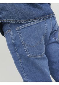 Vaqueros de denim en azul medio, con un diseño clásico de cinco bolsillos. Costuras de los bolsillos traseros en un sutil patrón de arco. Textura suave visible.