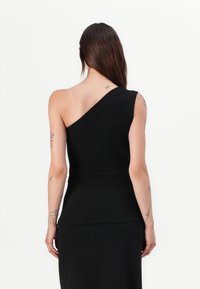 Svart ermeløs topp med asymmetrisk design, myk tekstur og tettsittende fasong, som møtes i livet med en glatt finish.