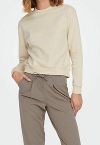 Felpa beige con collo tondo e polsini a costine, abbinata a pantaloni grigi con cordino in vita, dotati di tasche laterali e una vestibilità comoda.