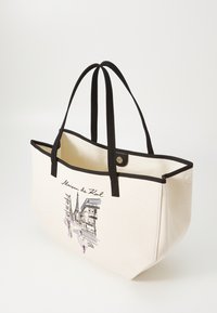 Borsa in tela color crema con rifiniture nere, che presenta un'illustrazione di una scena parigina e il testo "Maison de Karl." Manici neri robusti.