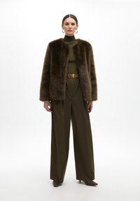 Brown faux fur coat with a relaxed fit, green turtleneck, wide beige pants, gold belt with an "M" buckle, and brown pointed-toe heels.