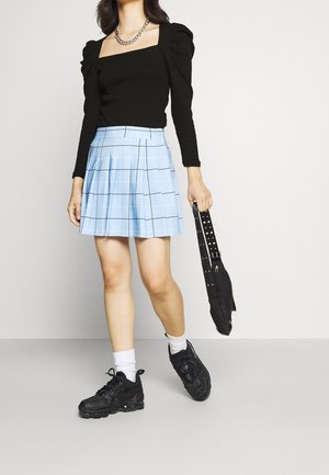 Schwarzes Langarmoberteil mit gepufften Schultern, hellblauter karierter Faltenrock, schwarze Sneakers und eine kleine schwarze Tasche mit Nieten.