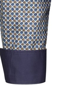 La manica della camicia a fantasia presenta un motivo geometricamente blu e marrone con un polsino blu scuro. Materiale in cotone con una texture morbida.