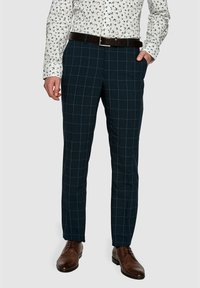 Granatowe spodni w kratę o dopasowanym kroju, wykonane z lekkiego materiału. Zawierają pasek z metalową klamrą w kolorze srebrnym oraz brązowe skórzane buty.