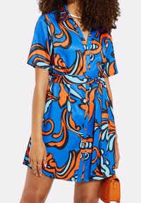 Kleid mit kurzen Ärmeln aus blauer Satin mit orangefarbenen und schwarzen abstrakten Mustern. Mit Knopfleiste und einem Bindegürtel in der Taille.