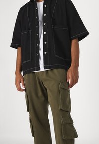 Svart kortärmad skjorta med vit söm och tryckknappar, lager på en vit t-shirt. Oljefärgad cargobyxa med flera fickor.