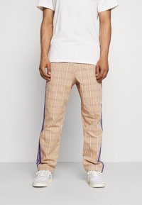 Beige ruudulised püksid siniste külgtriipudega, millel on mugav lõige ja sile kangatekstuur, koos valgete tossude ja T-särgiga.