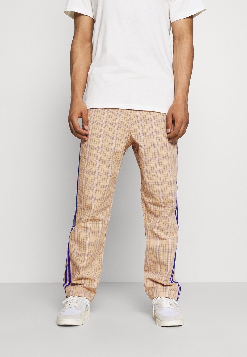 Beige ruudulised püksid siniste külgtriipudega, millel on mugav lõige ja sile kangatekstuur, koos valgete tossude ja T-särgiga.