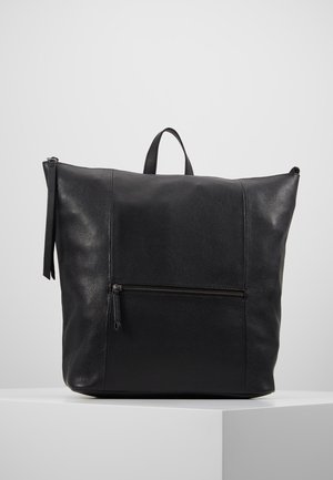 Schwarze, strukturierte Leder-Handtasche mit Tragegriff oben und vorderer Reißverschlusstasche, auf weißem Podest vor hellgrauem Hintergrund präsentiert.