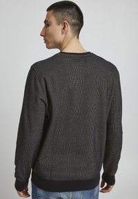 Sweatshirt noir pour homme avec un tissu texturé, un col rond et des poignets côtelés. Le dos présente un design simple sans motifs.