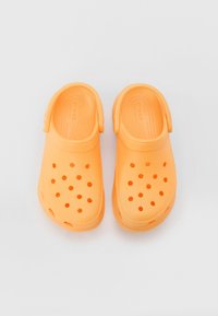 Sabots orange en matériau léger avec des trous de ventilation, une sangle arrière et une semelle texturée pour le confort.