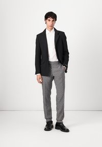Black blazer, white shirt, and patterned gray trousers with a diamond design; black shoes complete the outfit. Simple, clean lines throughout.