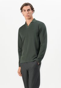 Mørkegrøn langærmet polo med V-hals, lavet af blødt stof; parret med gråstribede bukser. Minimalistisk design med rene linjer.