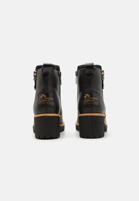 Bottines en cuir noir avec un extérieur texturé, présentant une semelle épaisse, une doublure en fourrure et un logo doré à l'arrière du talon.