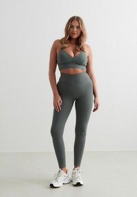 Sportieve set in gedempt groen, met een cropped bh-top en high-waisted legging. Het materiaal lijkt soepel en rekbaar, gecombineerd met witte sneakers.
