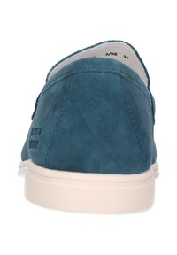 Zapatos slip-on de ante verde azulado con suela de goma blanca, caracterizados por una puntera redondeada y costuras mínimas. Nombre de la marca impreso en el talón.