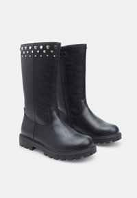 Stivali alti in pelle nera con zip laterale e dettagli borchiati a forma di cuore e rotondi lungo il bordo superiore. Suola spessa.